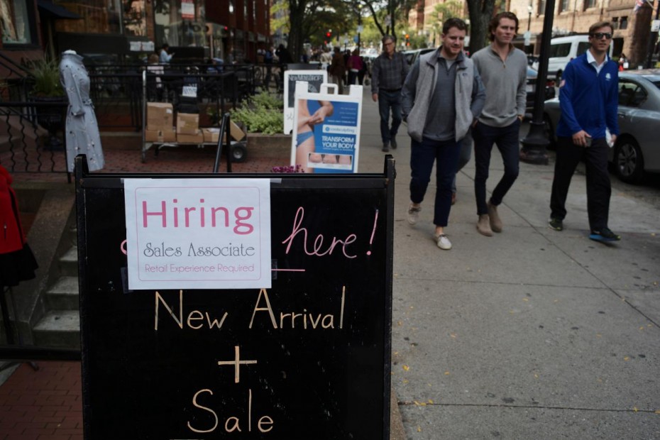 Pedestrians pass a sign advertising a sale and a job opening at a shop on Newbury Street in Boston