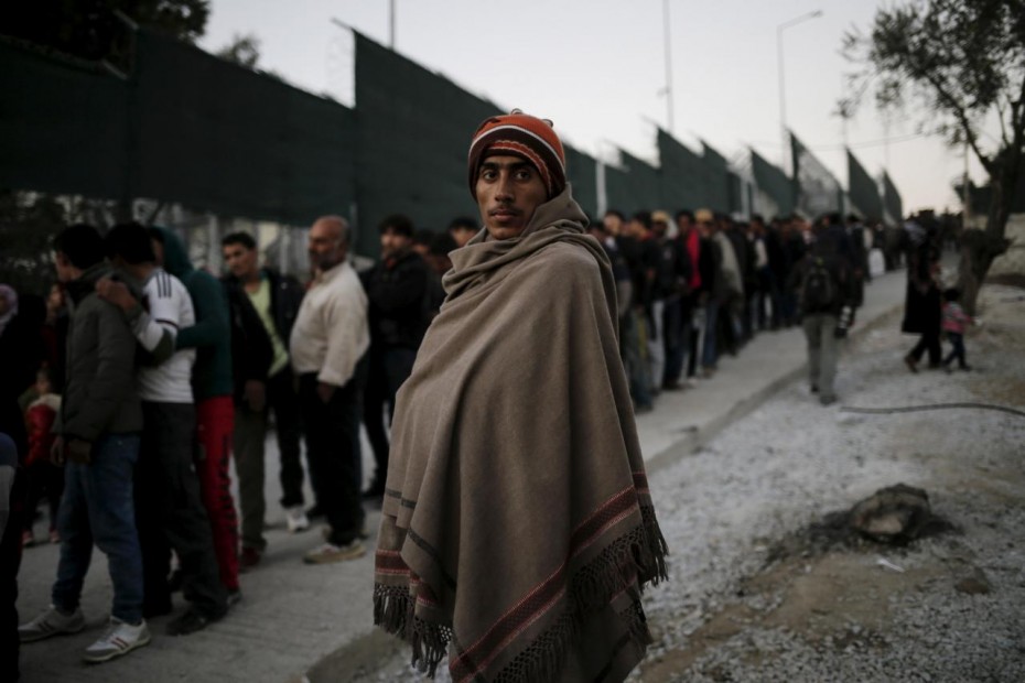 A migrant is covered with a blanket as refugees and migrants line up for a food distribution at the Moria refugee camp on the Greek island of Lesbos
