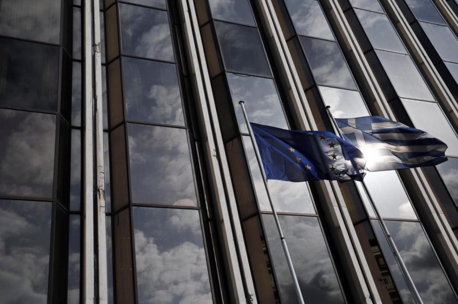 An EU and a Greek national flag flutter as the sky is reflected on a building front in Athens