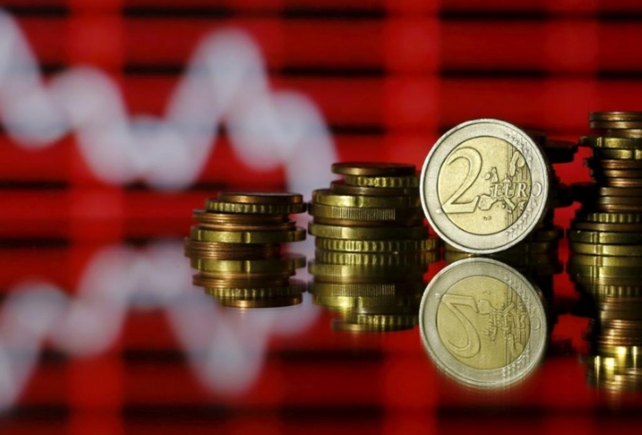 Euro coins are seen in front of a displayed stock graph in this photo illustration